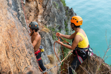 Asian man and woman climber climbing to rock mountain peak together at tropical island in sunny...
