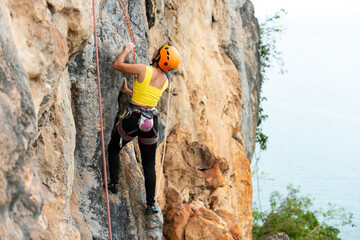 Confidence mature Asian woman climber with safety rope climbing on rocky mountain at tropical...