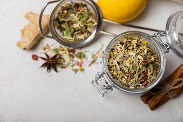 Fototapeta na wymiar Aromatic herbal tea in a glass jar on a light gray background. Tea set with lemon, cinnamon, ginger and anise. Immune and vitamin tea. Cold drink. 