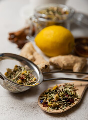 Dry herbal tea leaves in a strainer for brewing.Detox and immunity tea.Composition with lemon and ginger on a white cement background.