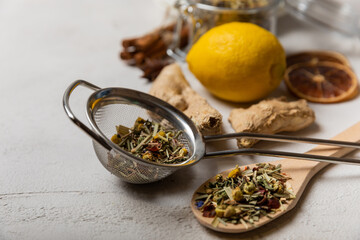 Dry herbal tea leaves in a strainer for brewing.Detox and immunity tea.Composition with lemon and ginger on a white cement background.