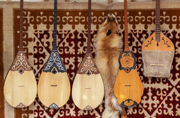 Kazakh national handmade musical instruments with horsehair strings hang on the felt wall of the yurt for sale.
