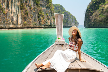 Young beautiful Asian woman in blue dress sitting on the boat passing island beach lagoon in summer...