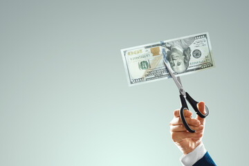 One hundred dollars bill is cut with scissors in the hand of a businessman. Business concept, income reduction, economic crisis, default, mortgage, loan, debt. copy space.