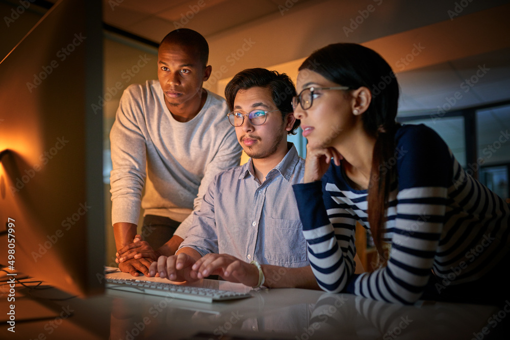 Poster Getting work done together. Shot of computer programmers working together late in the office.
