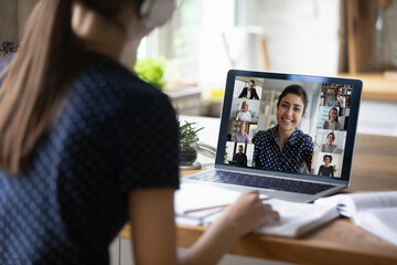 Fototapeta premium View over shoulder laptop screen view Indian teacher helps with assignment to young student girl sit at desk make exercise, take part in online video conference class. Video call event, study concept