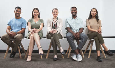 Confident and keen to prove their talent. Portrait of a group of businesspeople sitting together in a line against a white wall.