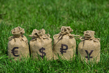 Sacks with symbols of chinese yuan, euro, american dollar, russian ruble on green grass