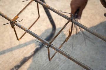 Construction workers securing steel rebar framing with hand wire are tying the beam steel for a construction site.