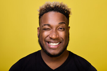 A handsome young man in a casual black T-shirt poses on a yellow background, smiles with a big...