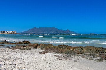 Fototapeta na wymiar Beach, rocks and ocean with Table Mountain in the background. Against a clear blue sky. 