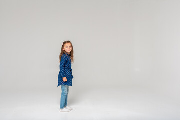 Full-size photo of a girl jumping and raising fists in a blue shirt and jeans, isolated on a white background, selective focus, motion