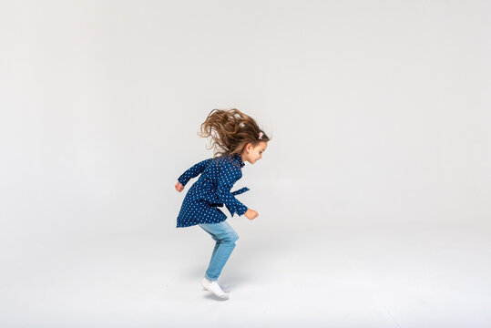 Full-size photo of a girl jumping and raising fists in a blue shirt and jeans, isolated on a white background, selective focus, motion