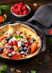 Dutch baby pancake with berries and icing sugar in a iron cast pan. Morning breakfast