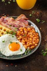 Potato waffles with fried egg, bacon and baked beans. Morning breakfast