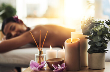 Indulge in a spa day. Shot of spa essentials on a table with a woman getting a massage in the background.