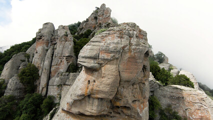 Aerial view of unusual rock formations and green green grass. Action. Fog and clouds and the mountain tops, beauty of nature.