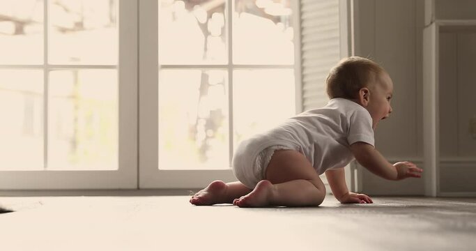 Energetic little baby boy girl about 6 months dressed in diaper white cotton singlet move crawl by warm wooden floor with underheating. Funny babe child make first attempts to discover world around
