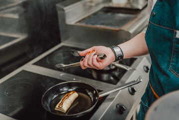 chef hand cooking Thin pancakes crepe rolls with ground meat in pan at a restaurant kitchen