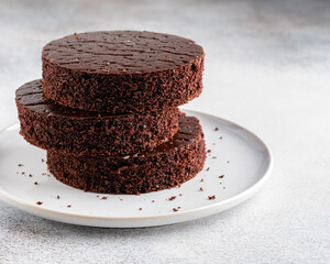 Chocolate sponge cake (biscuit) cut in circle layers stacked on ceramic plate with crumbs. Sponge...