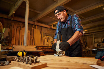 Senior Professional carpenter in uniform working of manual milling machine in the carpentry workshop