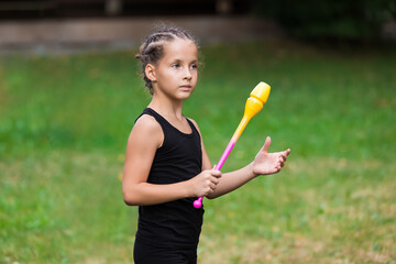 Portrait of serious girl on rhythmic gymnastics training with clubs in summer in sports camp...