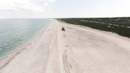 Aerial view of a tractor on the tropical beach with white sand. Action. Machine driving on beautiful shore with greenery and ocean.