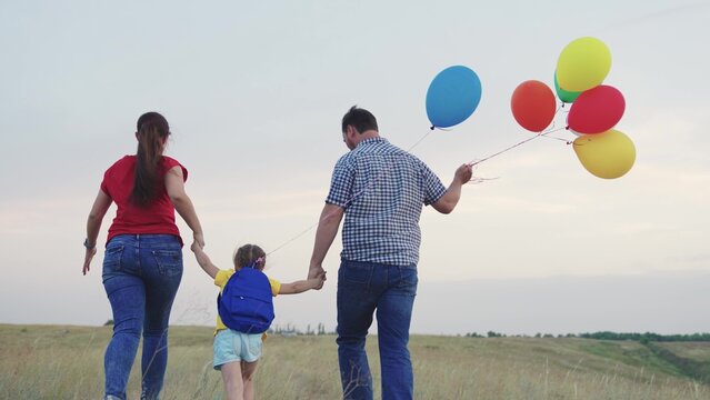 child kid runs with mother father with beautiful colorful balloons. happy family concept. group people running across field with helium colored balloons. happy family running green field together.