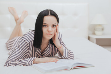 Barefoot young teenage girl looking at the camera lying on her bed reading a book