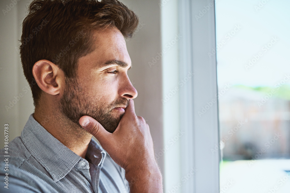 Poster what can he be thinking about. shot of a focused young man looking through a window while contemplat