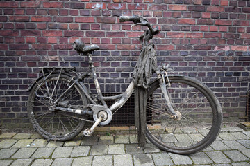 Fototapeta na wymiar Bicycle covered in mud and silt, dredged out of canal or river, standing or parked against orange brick wall