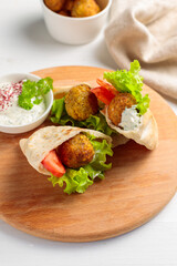 Two mini pitas with falafel, sauce and fresh vegetables. Close-up, on a round wooden board.