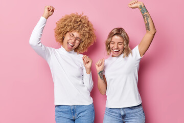 Horizontal shot of cheerful upbeat women dance carefree dressed in white t shirts and jeans move...