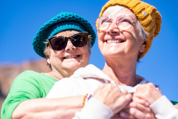 Happy couple of mature elderly women wearing glasses and hats hug laughing. Smiling carefree senior...