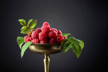 Fresh raspberries with leaves in an old brass dish.