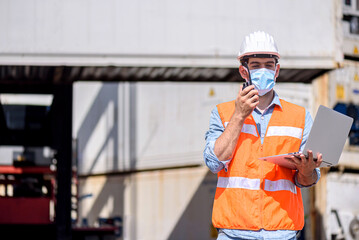 	
Confident Caucasian man engineer wearing white safety helmet using computer laptop and check for control loading containers box from Cargo freight ship for import and export, transport