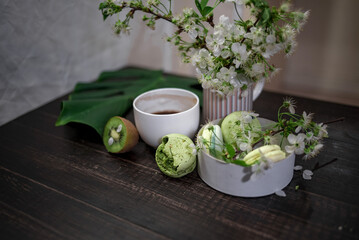 Green and beige macaroons tied with a tourniquet against the background of cherry blossom branches on a wooden table