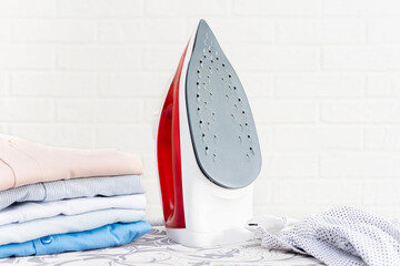 Close-up of a steam iron and a stack of washed folded clothes on an ironing board. The concept of...
