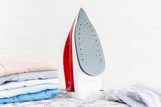Close-up of a steam iron and a stack of washed folded clothes on an ironing board. The concept of household chores, daily routine, cloth care.