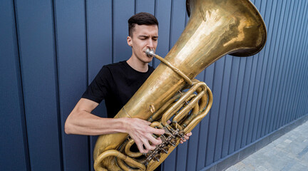 Young street musician playing the tuba near the big blue wall