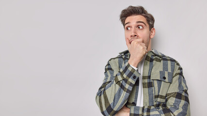 Shocked young European adult man stares bugged eyes covers mouth with hand wears checkered shirt...