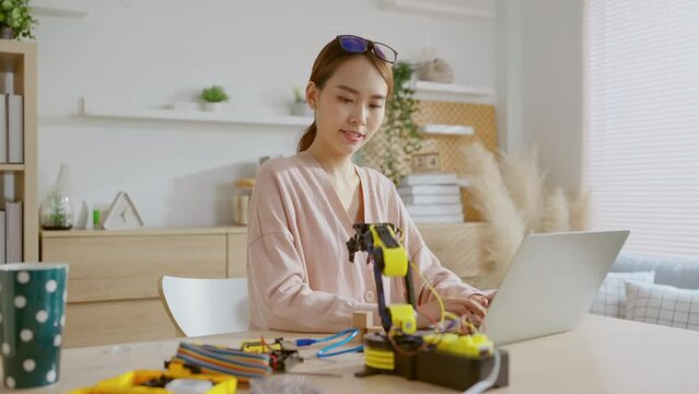 smart asian female programer learning robot arm ai coding electronic board cable in STEM, STEAM she try to testing her autonomous  robotic arm with sensors via Arduino platform at home