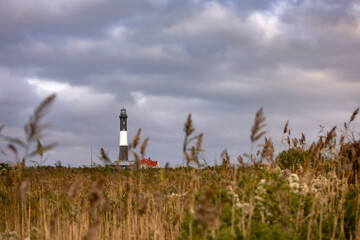 Dramatic storm clouds overhead a tall stone lighthouse with beach grass in the foreground. Fire Island, Long Island New York