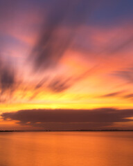 Obraz premium Beautiful warm colors light up sweeping clouds in the sky just after sunset over a glassy still body of water. Jones Beach - Long Island New York