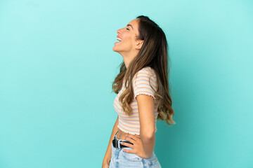 Young woman over isolated blue background laughing in lateral position