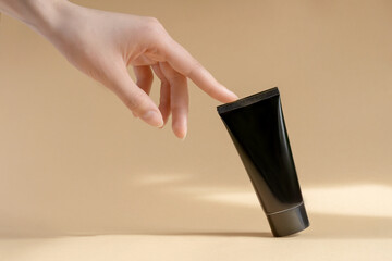 Woman's hand touches a mockup of black tube of cream. Unmarked packaging for cosmetics in sunlight...
