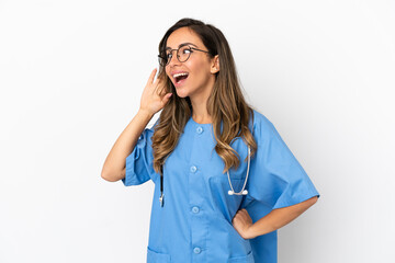 Young surgeon doctor woman over isolated white wall listening to something by putting hand on the ear