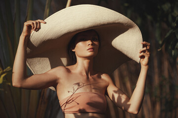 Sun bathing woman in straw hat portrait. Palm tree shadows on the body. Health tanning concept