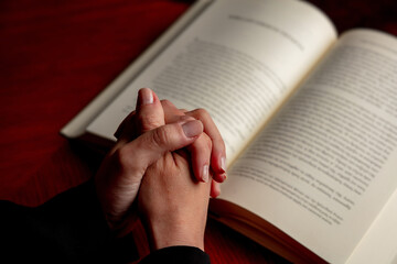 Fototapeta premium Pray to God. Female hand in prayer over a Holy Bible, wooden table, close up view.