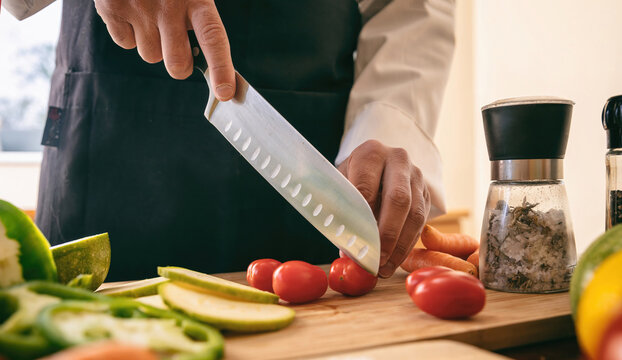 Chef cut tomato with a knife on a chopping board, close up. Fresh vegetable on kitchen table. - Powered by Adobe